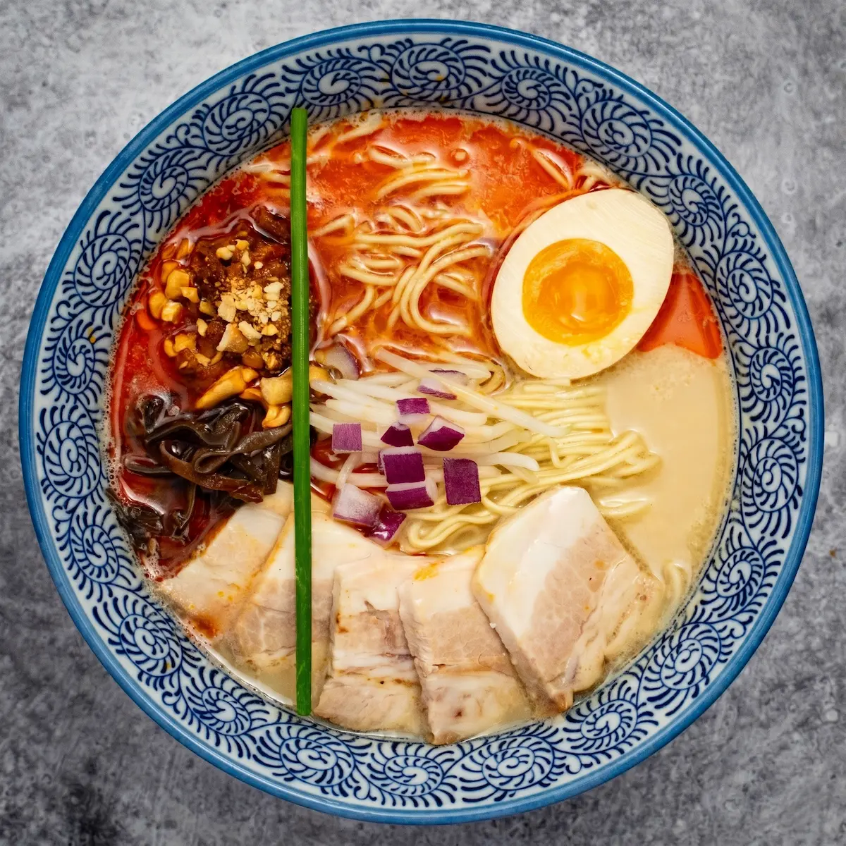 Tonkotsu Spicy - A bowl of spicy pork broth ramen with medium straight noodles, pork chashu, ground pork bomb, kikurage mushroom, bean sprouts, cashews, and a soft-boiled egg
