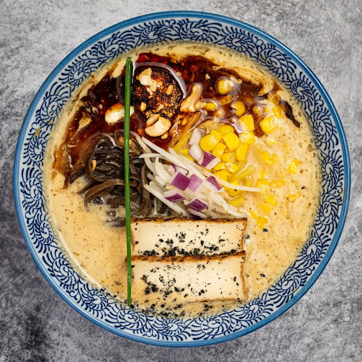 Vegan Miso Spicy - A bowl of spicy miso and sesame broth ramen with thick noodles, tofu chashu, black garlic oil, bean sprouts, corn, kikurage mushrooms, spice bomb, and cashews