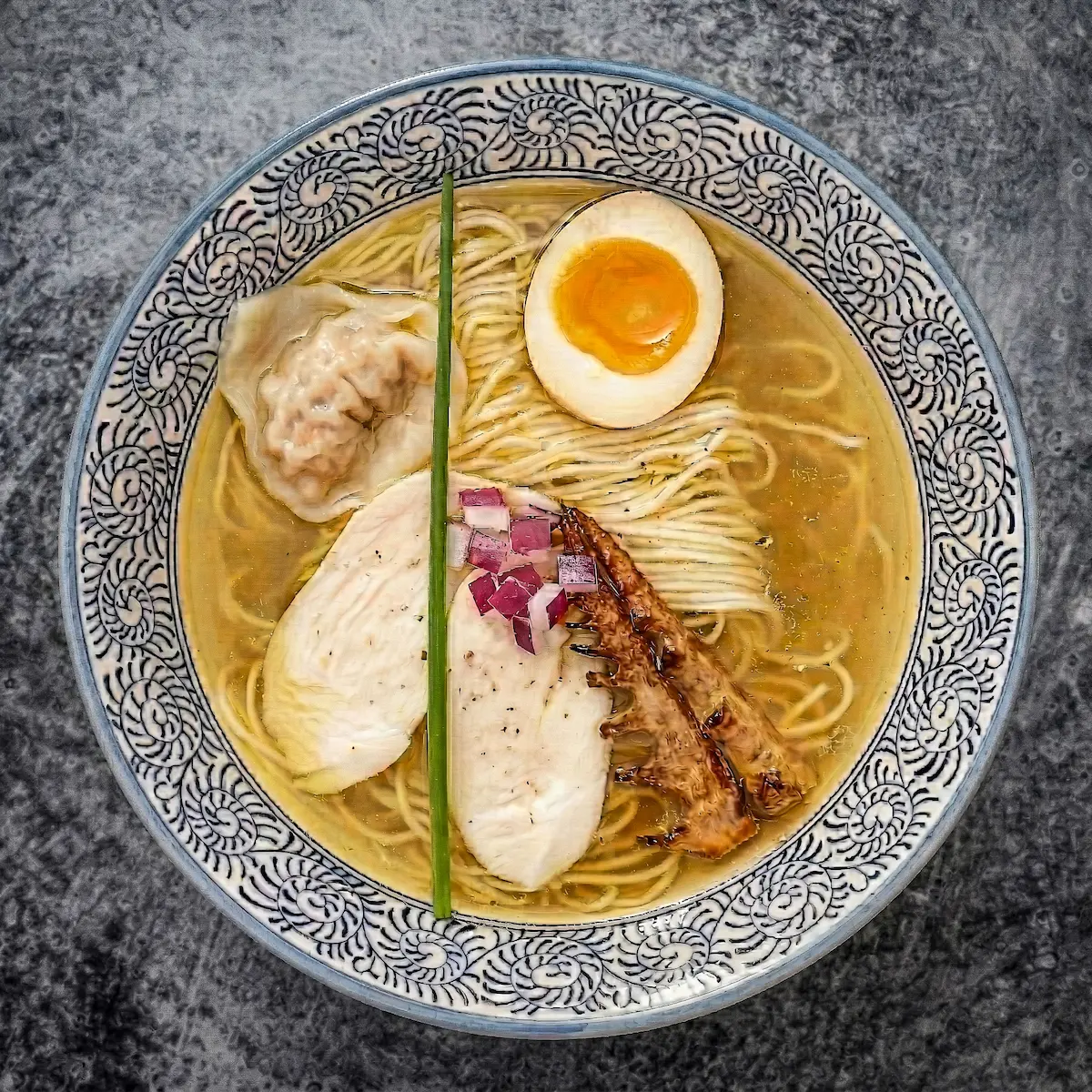 Yuzu Shio - A bowl of golden clear chicken broth ramen with thin noodles, yuzu citrus aroma, bamboo shoots, chicken breast chashu, jalapeño chicken wantan, and a soft-boiled egg